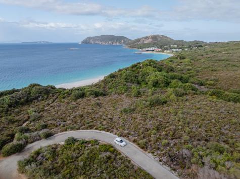 Aerial view of a car on a road winding through bushland with a beach and ocean in the distance